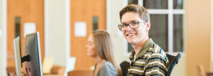 Male Student with glasses sitting at a computer smiling